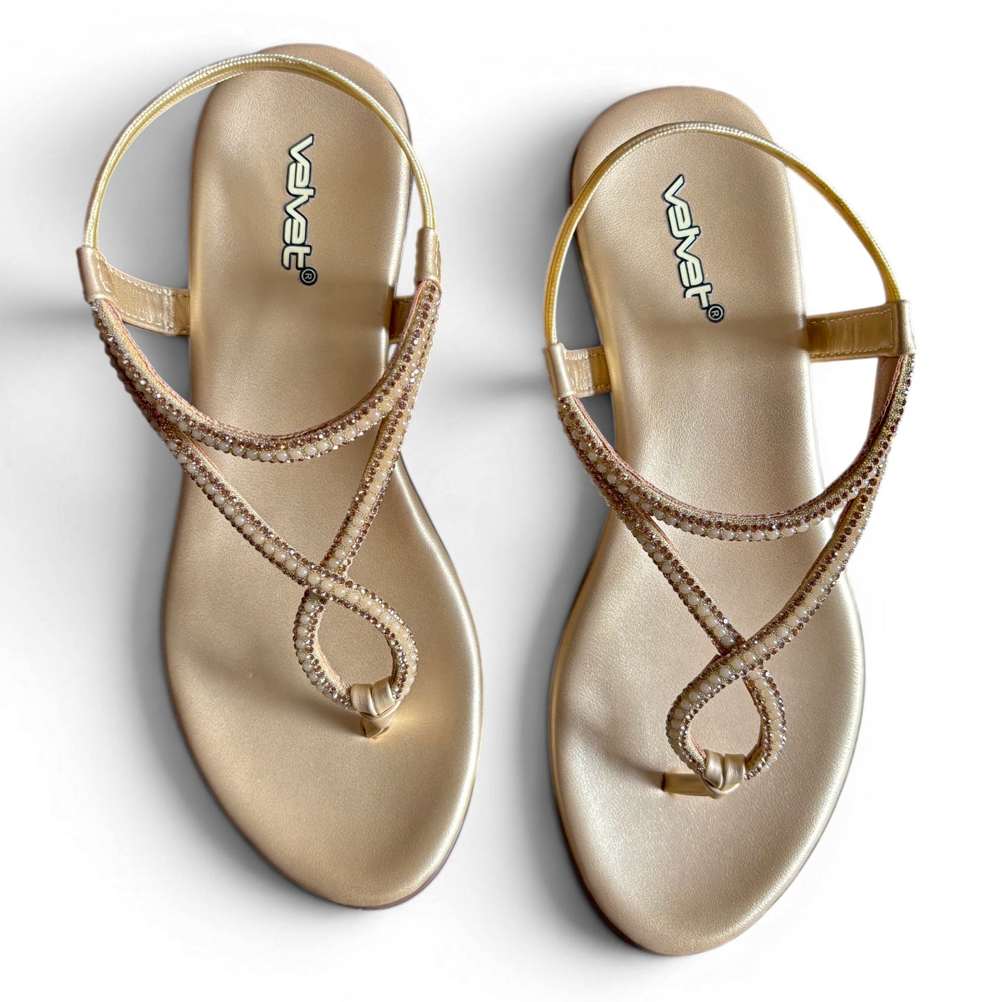 A pair of metallic gold flat sandals with criss-cross rhinestone-embellished straps, shown from a top-down view on a white background. The brand name 'VAVET' is printed on the footbed.